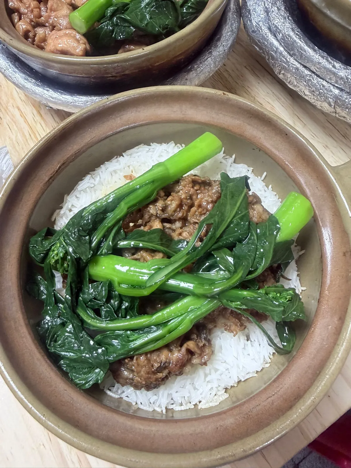 打開咗蓋嘅瘦肉煲仔飯特寫，面頭堆滿油亮嘅菜心，中間係深褐色嘅碎瘦肉，四周露出嚟嘅米飯全部係白色，見唔到豉油汁滲落飯度；左上角係另一煲雞飯