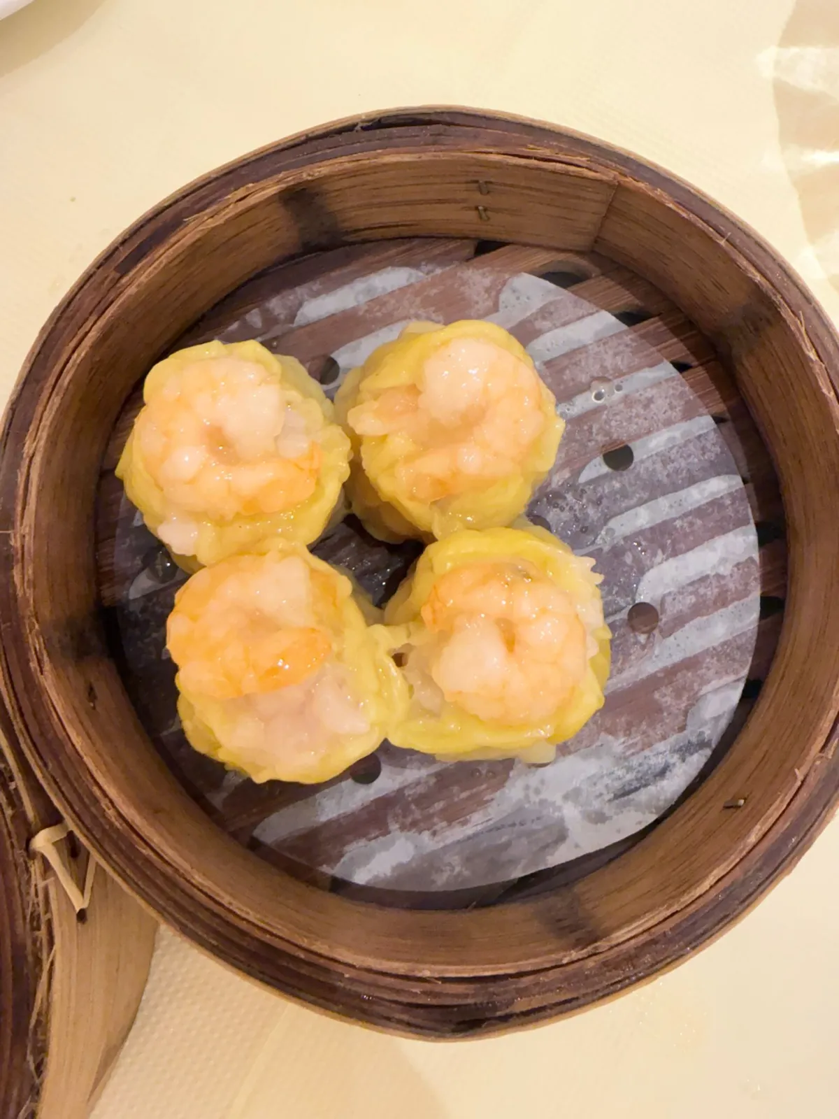 竹蒸籠入面四粒燒賣，黃色薄皮包住豬肉餡，每粒面頭放一隻剝好殼嘅蝦，蝦肉透白帶橙紅邊；籠底墊住一張蒸紙