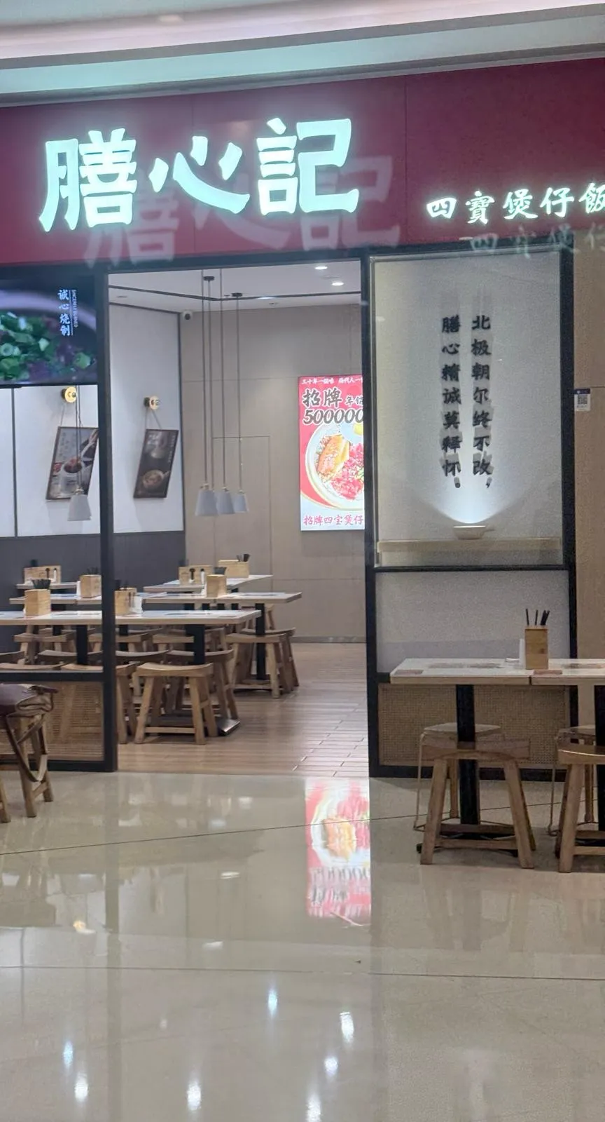 商場入面嘅店面：暗紅色招牌上「膳心記」三個白色發光大字，右邊細字寫「四寶煲仔飯」，左邊有圓形店徽；招牌下面係玻璃門面，望入去見到淺色木枱同圓凳，牆上掛住菜式相片同一張招牌煲仔飯海報