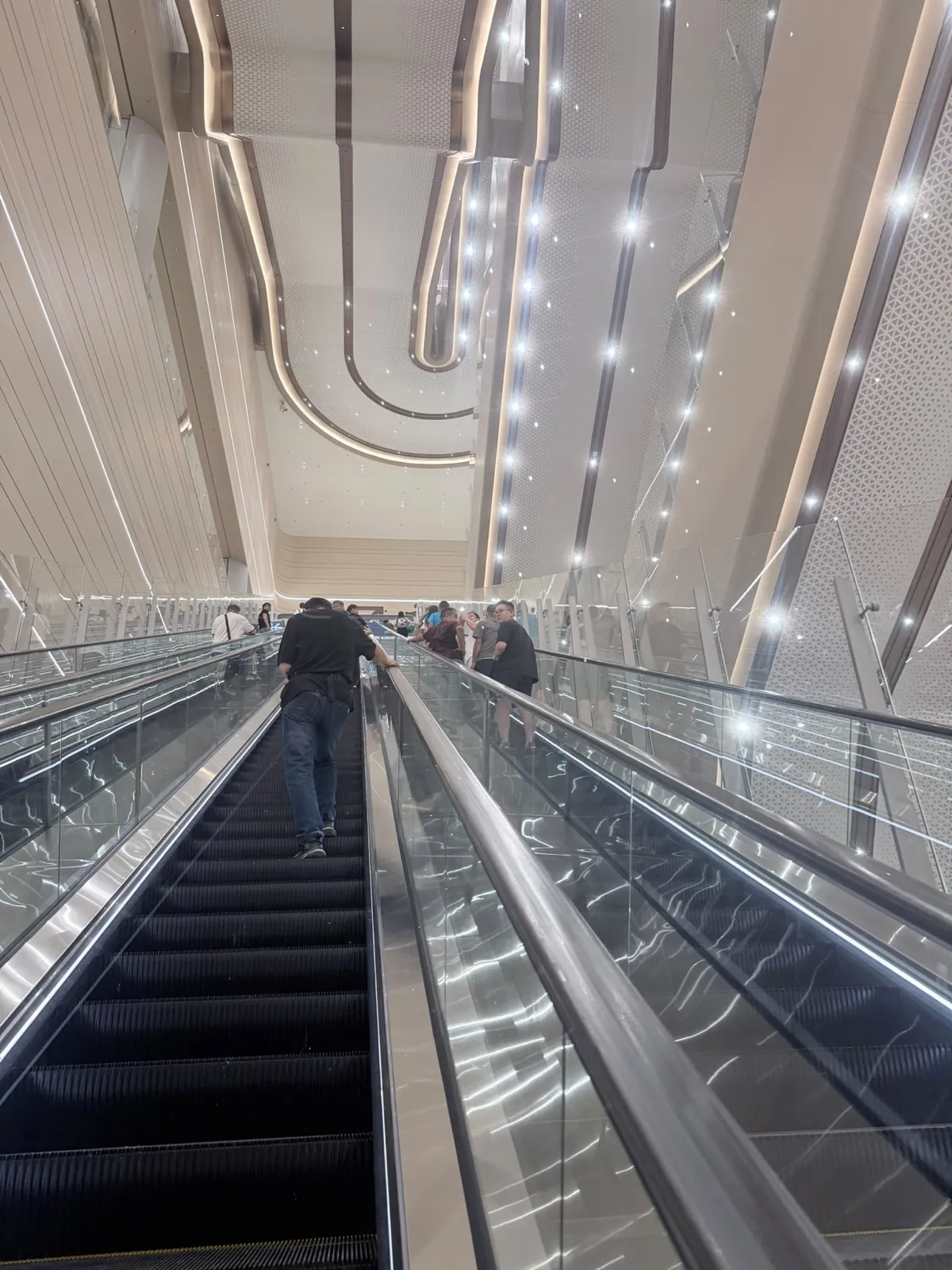 新皇崗口岸一組很長的扶手電梯向上，玻璃欄杆，天花板有彎曲燈槽