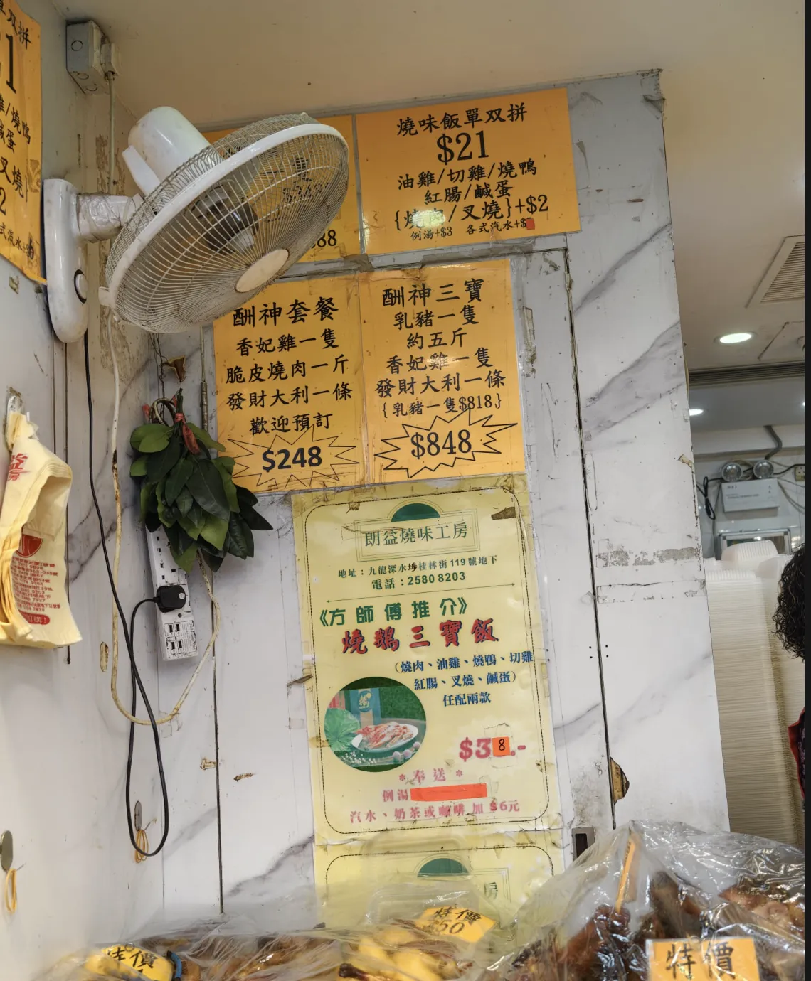 朗益燒味工房牆上的餐牌，寫有燒味飯單拼或雙拼價錢，以及燒肉和叉燒加價；下方海報列出店名、地址和電話