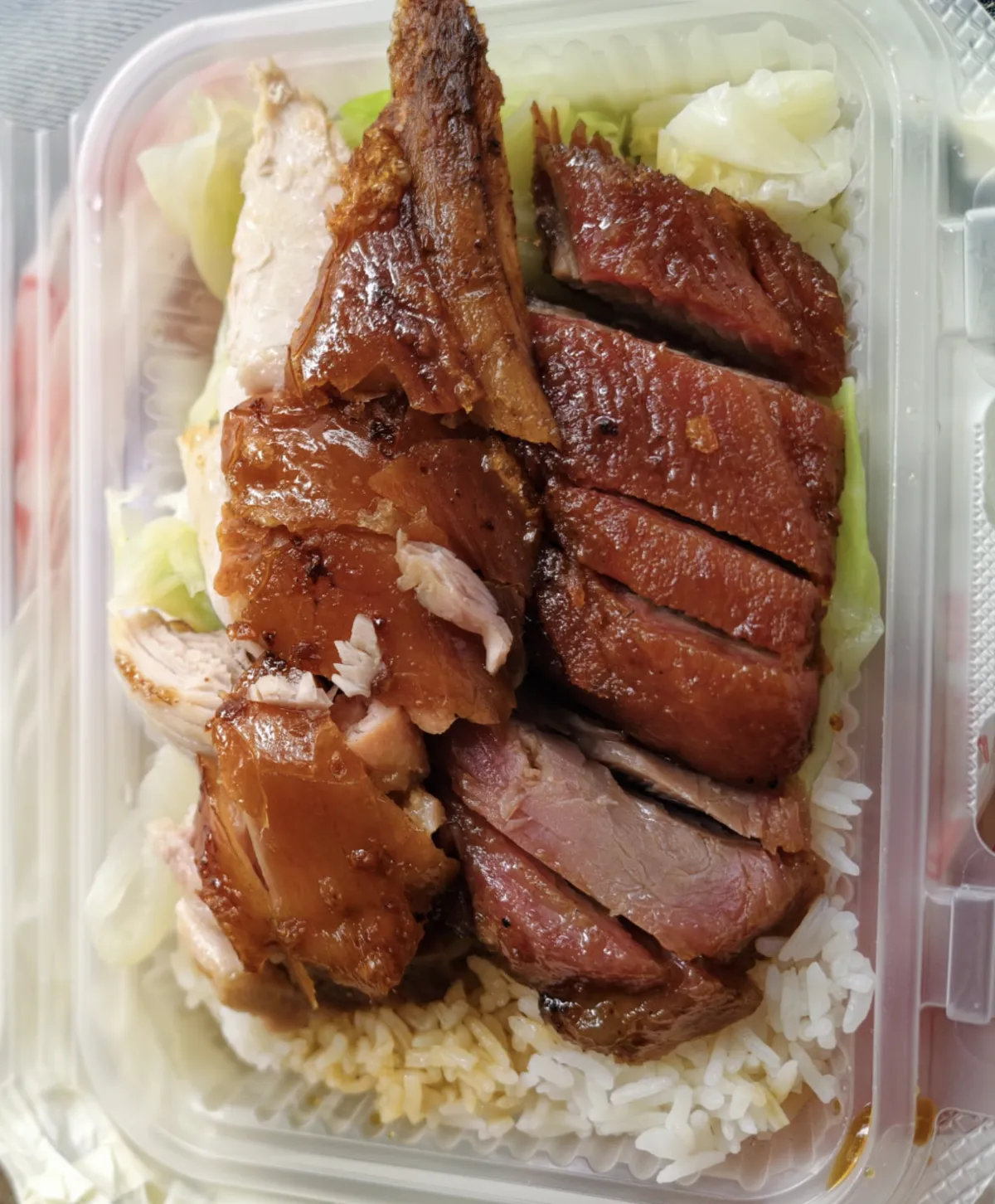外賣飯盒裡有白飯、生菜和切片燒肉、叉燒，兩款燒味鋪在飯面上