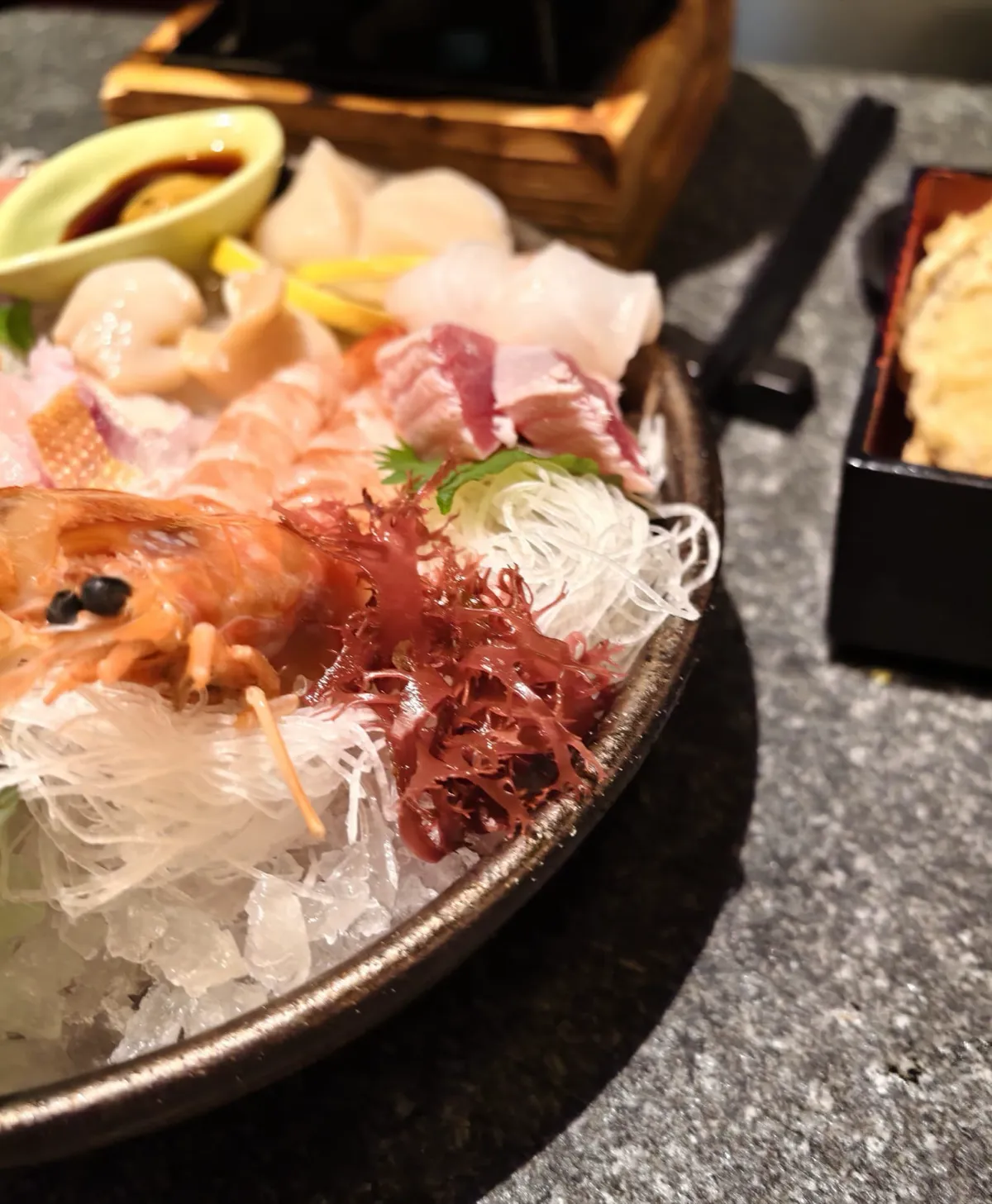 近鏡一碗刺身：甜蝦、白蘿蔔絲、紅色海藻、扇貝同金槍魚放喺碎冰上，旁邊有一碟醬油